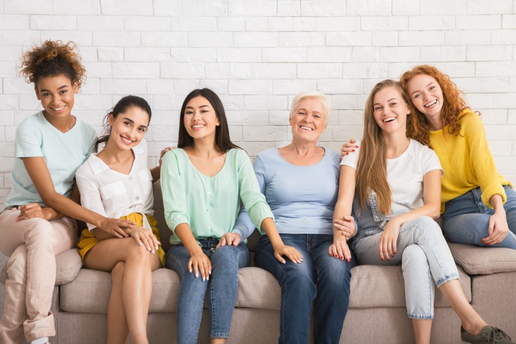 groupe-de-femmes-souriant-assises-sur-un-canapé-contre-un-mur-blanc